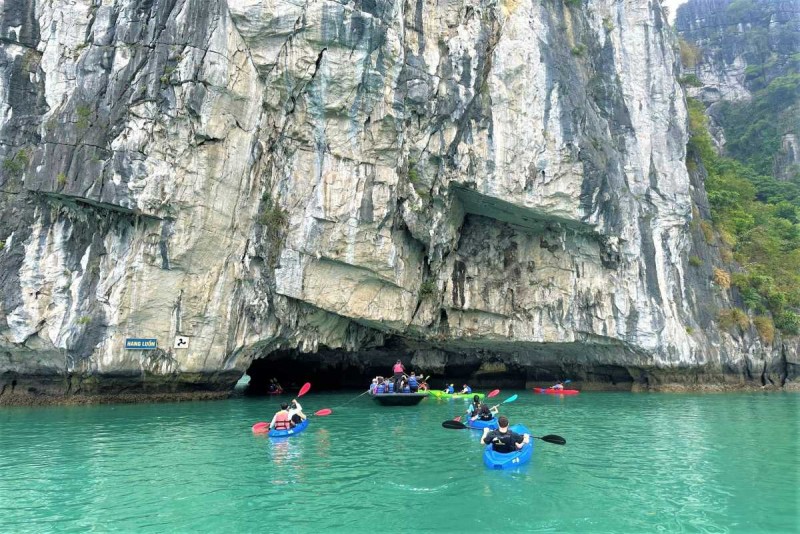 Bamboo Boat Ride Luon Cave Halong Bay cruising near cliffs Bamboo boat with tourists cruising near towering limestone cliffs at Luon Cave, Halong Bay surrounded by green vegetation