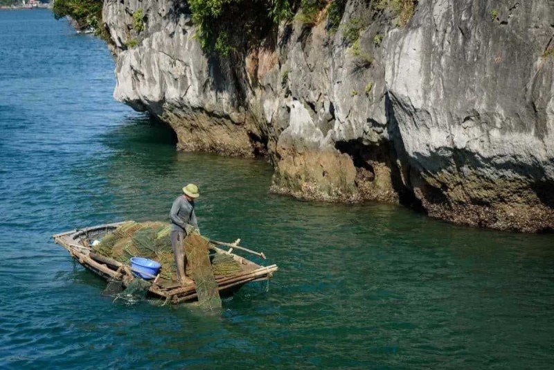Bamboo Boat Ride Vung Vieng Fishing Village traditional fishing boat Traditional fishing boat moored near floating homes at Bamboo Boat Ride Vung Vieng Fishing Village amidst scenic limestone cliffs.