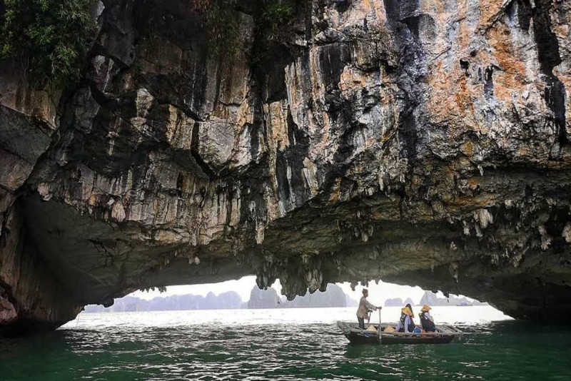 Boat entering limestone cave in Halong Bay Bamboo boat rowed under a limestone arch with passengers heading toward a cave in Halong Bay