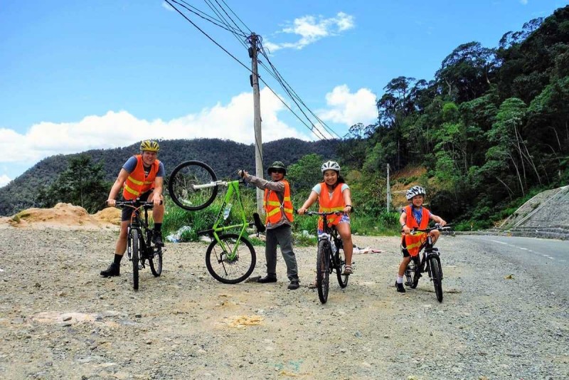 Family cycling tour on a gravel mountain road A family of four with a guide cycles a gravel road in the Nha Trang highlands with forested backdrops