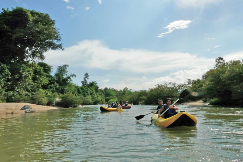 Guided Kayak Group Tour on Cai River Groups of tourists paddling inflatable kayaks through a calm river bend with thick green foliage.