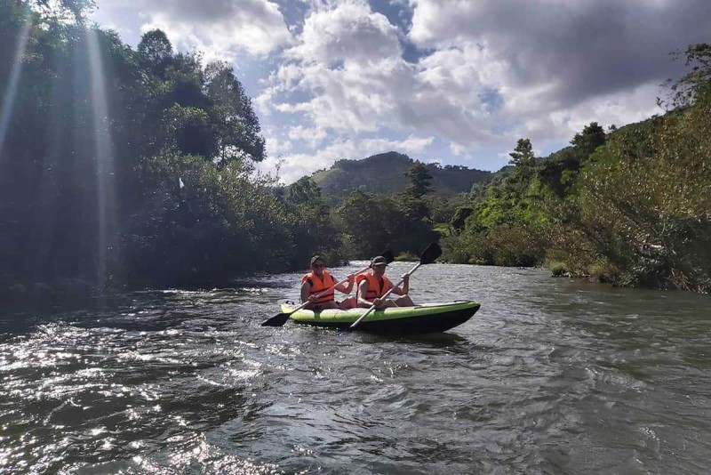 Kayaking through Jungle Rivers in Nha Trang Two kayakers paddling under dramatic sunlight and cloudy sky surrounded by dense riverside jungle.