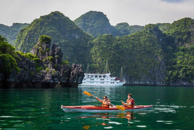 Kayaking Cong Do Island Bai Tu Long Bay couple kayaking Kayaking Cong Do Island Bai Tu Long Bay shows a smiling couple kayaking together wearing life jackets with dramatic cliffs nearby.