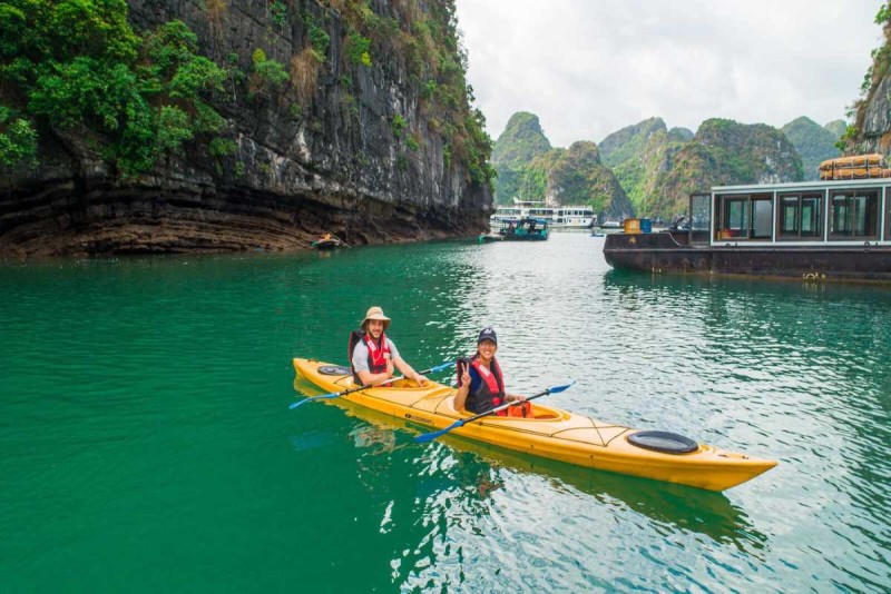 Kayaking Cong Do Island Bai Tu Long Bay couple enjoying nature Kayaking Cong Do Island Bai Tu Long Bay captures a couple paddling together with lush green cliffs in the background under clear skies.