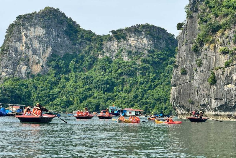 Kayaking Cua Van Halong Bay alongside traditional boats Kayaking Cua Van Halong Bay near traditional wooden boats moored at floating village homes amid green cliffs