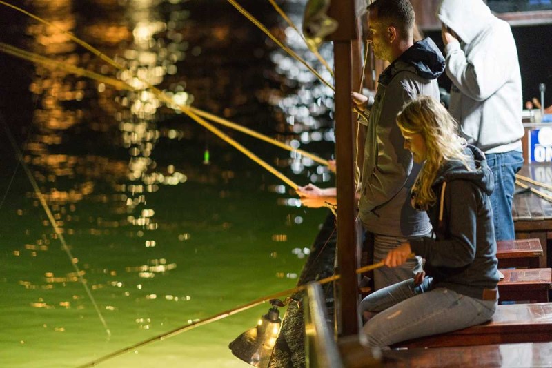 Squid Fishing Halong Bay Nighttime Squid Catch Man holding up a freshly caught squid on a fishing line during a nighttime squid fishing tour.
