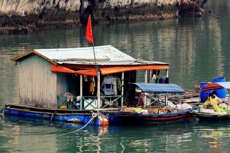 Traditional floating house with Vietnamese flag Cua Van Village Traditional floating house flying the Vietnamese flag at Cua Van Village in Halong Bay, with clothes drying on the porch