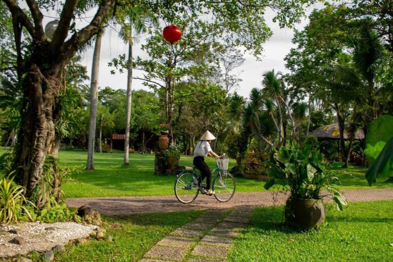 Local cycling through a village garden path A local cyclist wearing a conical hat rides along a garden path surrounded by tropical trees near Nha Trang
