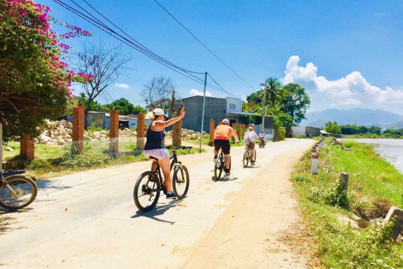 Group ride on rural village roads near Nha Trang Group of cyclists ride along a sunny rural road lined with houses and green riverbanks near Nha Trang