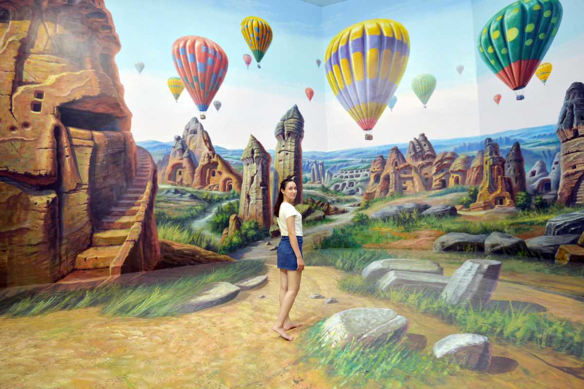 3D Museum Art in Paradise Da Nang hot air balloon landscape mural 3D Museum Art in Paradise Da Nang presents a visitor among colorful hot air balloons and ancient rock formations in a scenic mural landscape.