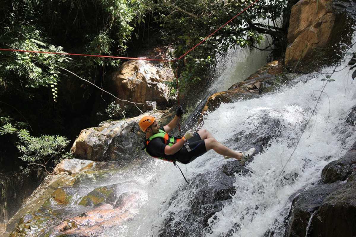 Adventure Canyoning at Datanla Waterfalls Da Lat Adventurer rappelling down a waterfall at Datanla Waterfalls in Da Lat wearing safety gear and helmet