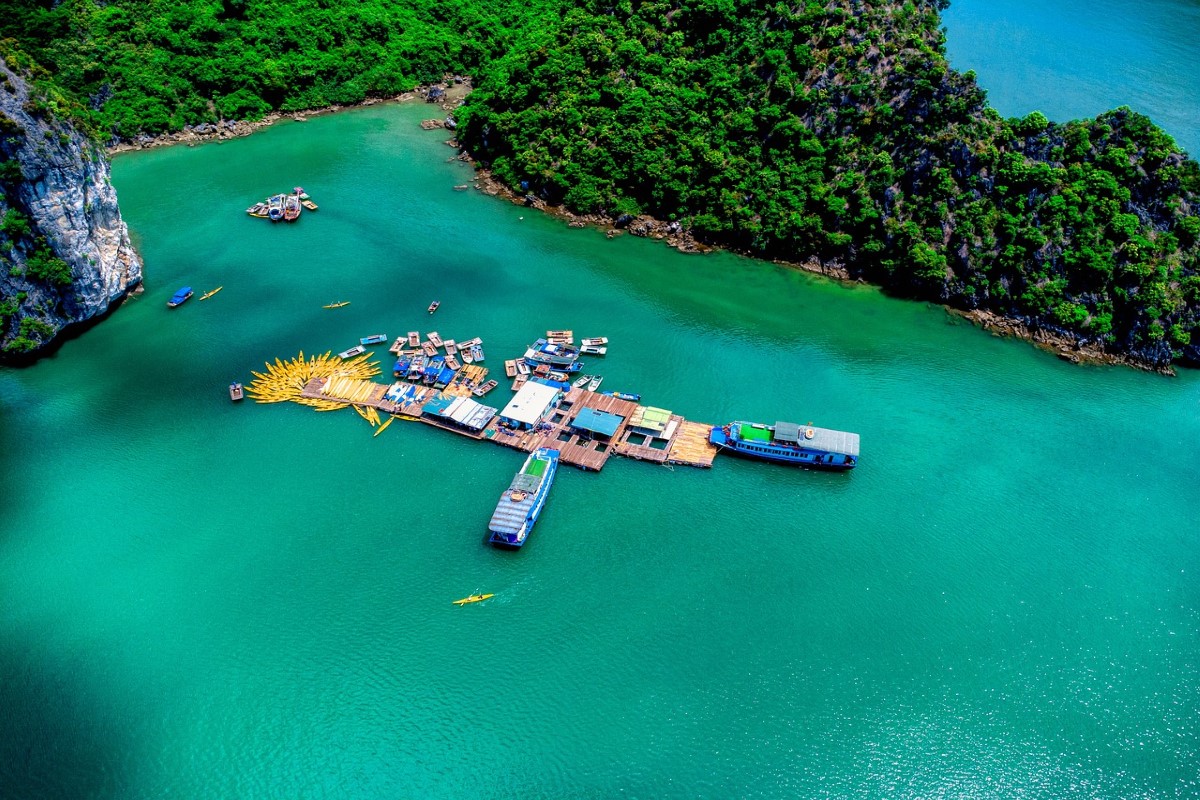 Aerial view of Cong Do Island's floating fishing village surrounded by emerald waters and green cliffs.