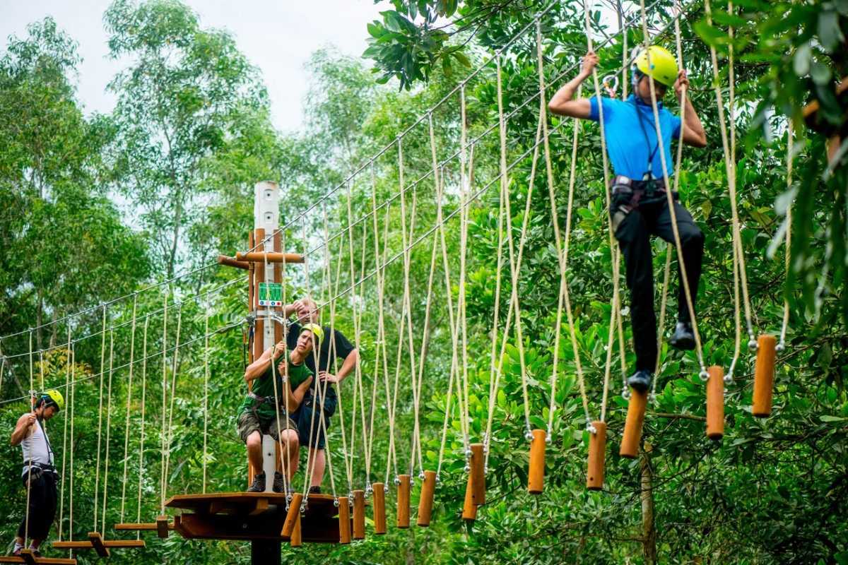 Highwire Adventure Course at Alba Thanh Tan Visitors wearing helmets navigating the highwire rope adventure course in forest at Alba Thanh Tan