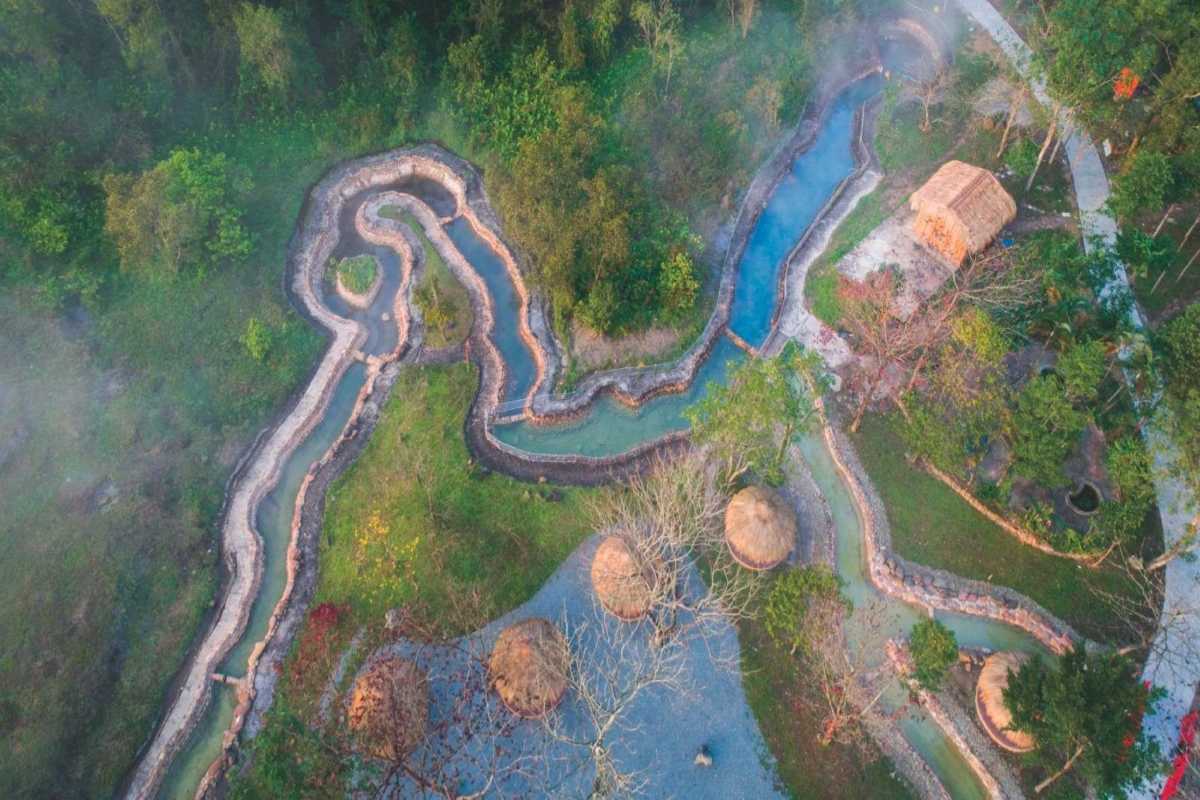 Hot Spring River Flow at Alba Thanh Tan Aerial view of winding hot spring river with steam rising, surrounded by greenery and huts