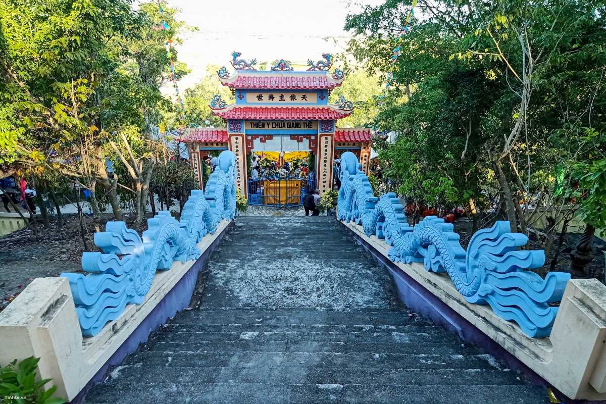 Stone staircase leading to Am Chua Temple flanked by blue dragon sculptures in a lush forest setting.