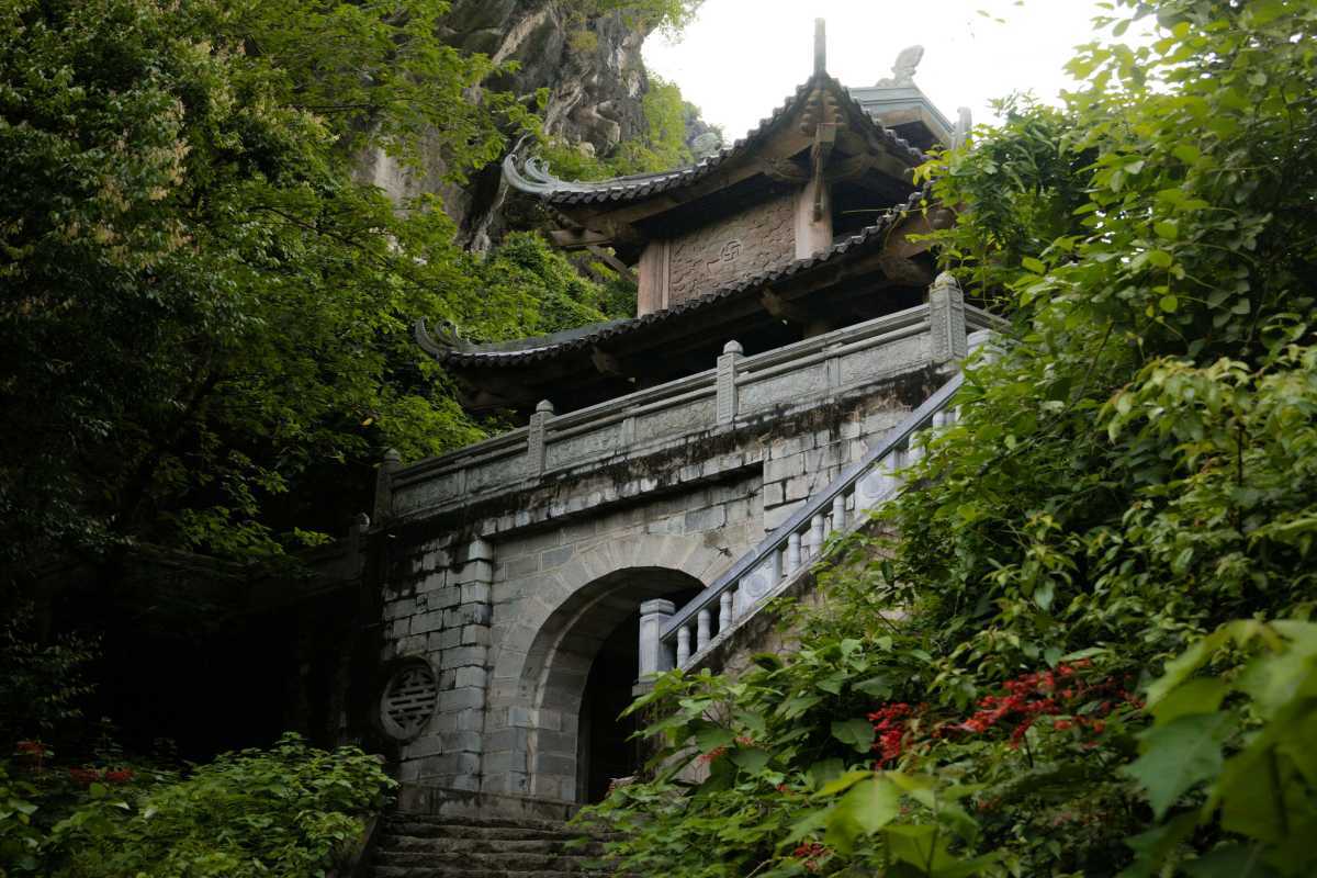 Am Tien Cave Ninh Binh ancient stone gate and stairway Am Tien Cave Ninh Binh stone gate and stairs lead through forest and limestone cliffs to entrance.