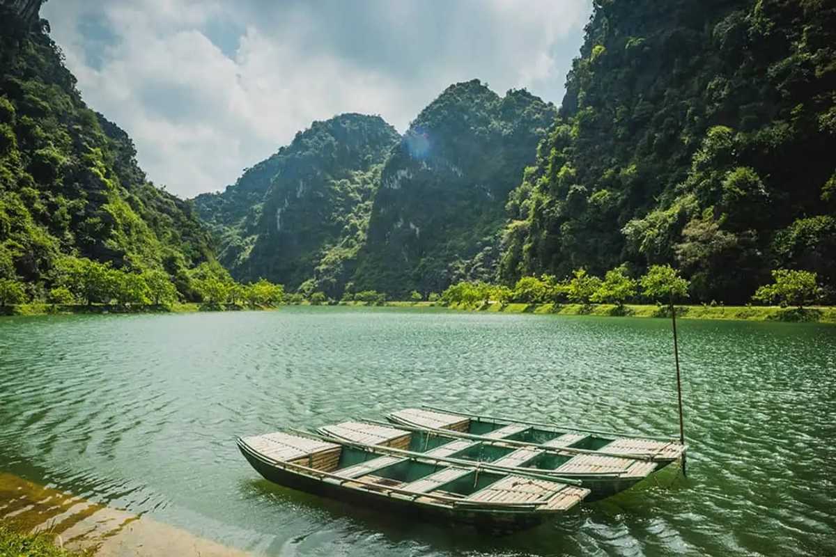 Am Tien Cave Ninh Binh emerald lake surrounded by cliffs Am Tien Cave Ninh Binh emerald lake calm, surrounded by forest and rugged limestone cliffs.