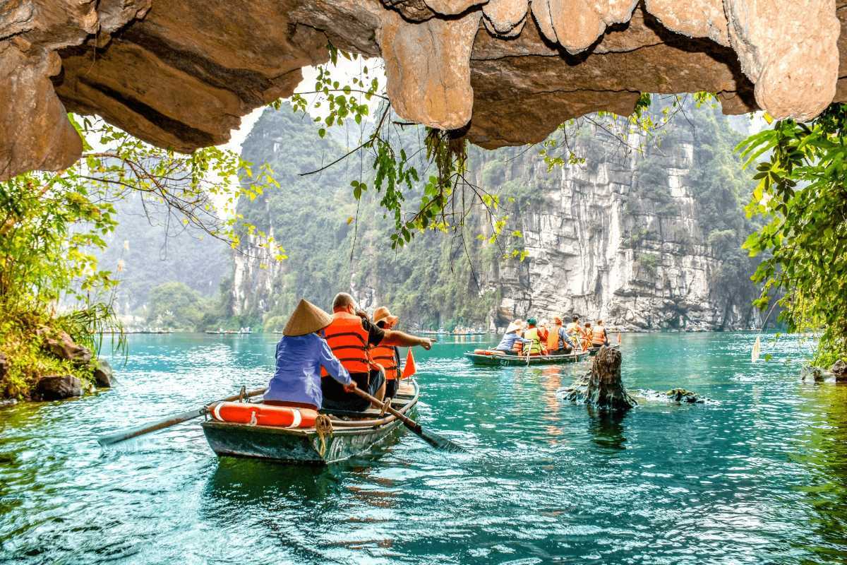 Am Tien Cave Ninh Binh lake boat ride limestone cliffs Am Tien Cave Ninh Binh visitors ride boat across jade lake, surrounded by towering limestone cliffs.