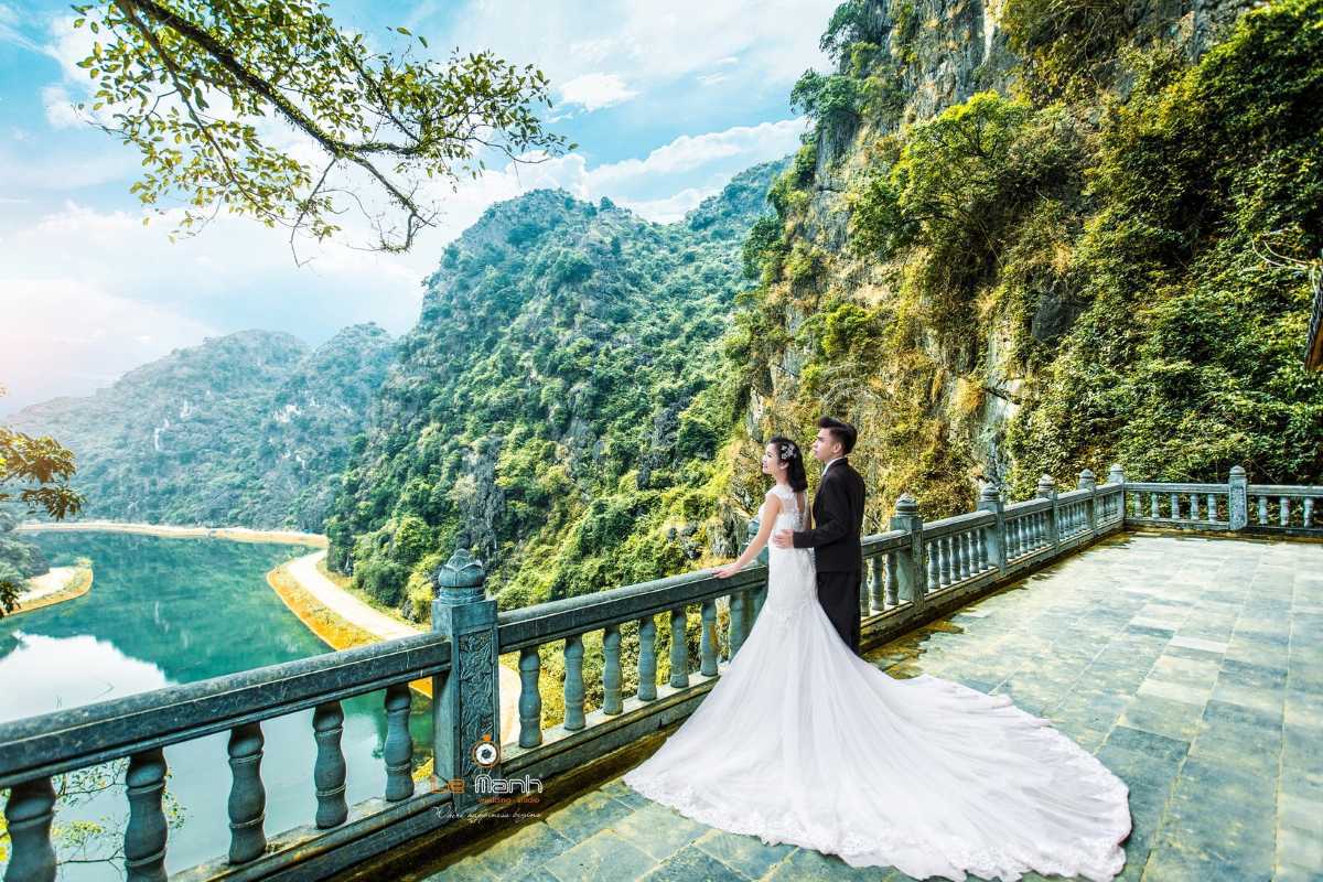 Am Tien Cave Ninh Binh panoramic lake wedding photoshoot Am Tien Cave Ninh Binh couple in wedding attire on balcony above lake and limestone hills.