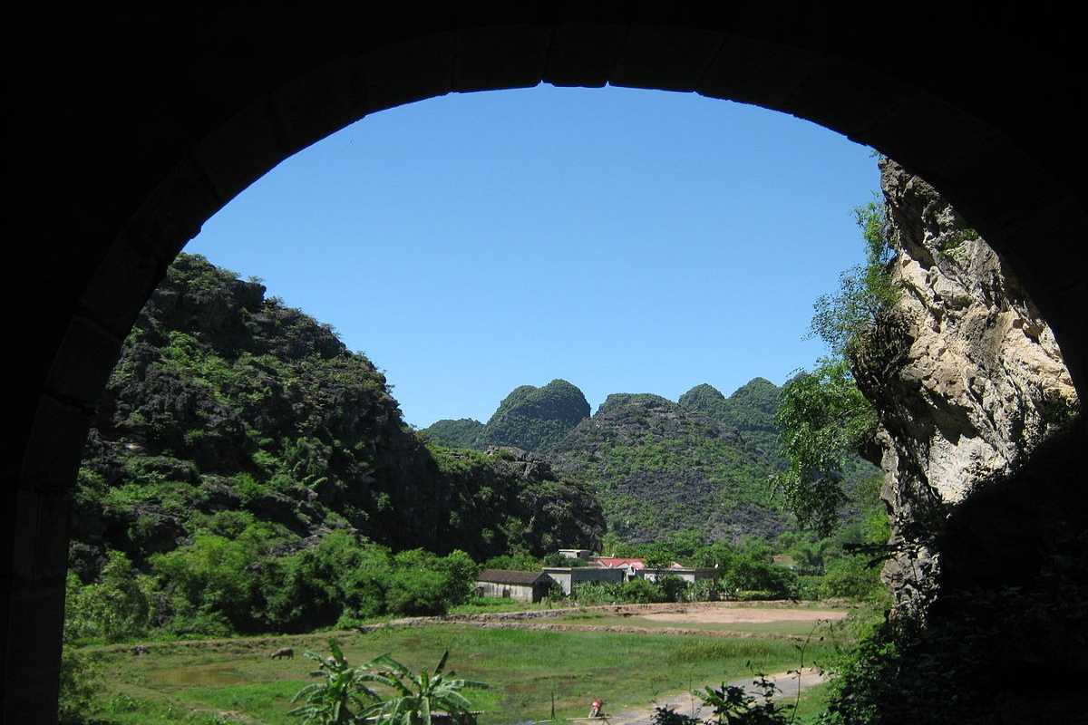 Am Tien Cave Ninh Binh scenic entrance valley view Am Tien Cave Ninh Binh entrance shows lush valley, limestone mountains, and distant village under sky.