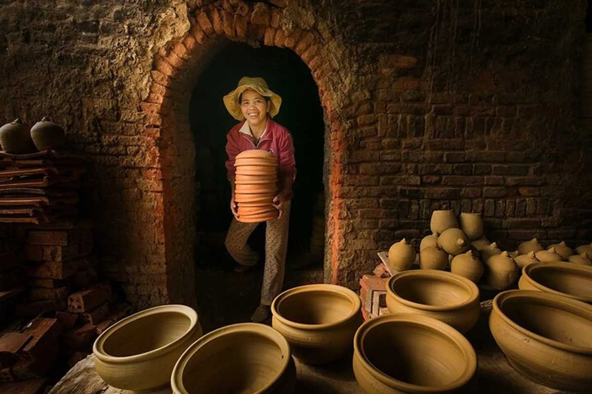 Artisan Carrying Pottery Out of Traditional Kiln Smiling artisan removing freshly fired pottery from a brick kiln at Thanh Ha Pottery Village