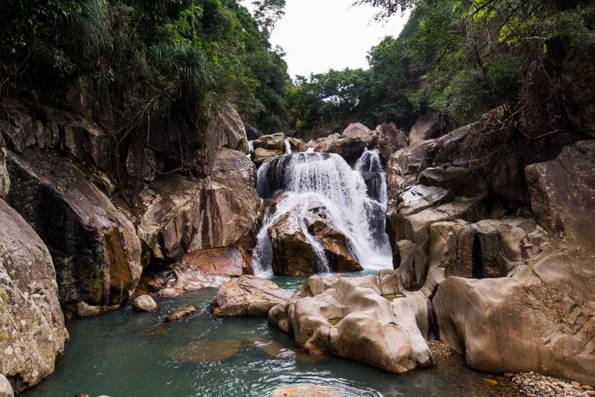 Second waterfall level at Ba Ho Wide shot of the second tier of Ba Ho Waterfalls in Nha Trang surrounded by boulders and lush trees.