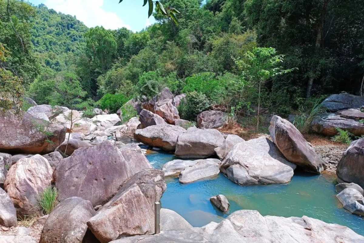 Calm turquoise stream at Ba Ho Turquoise water winding between boulders at Ba Ho Waterfalls under clear skies.