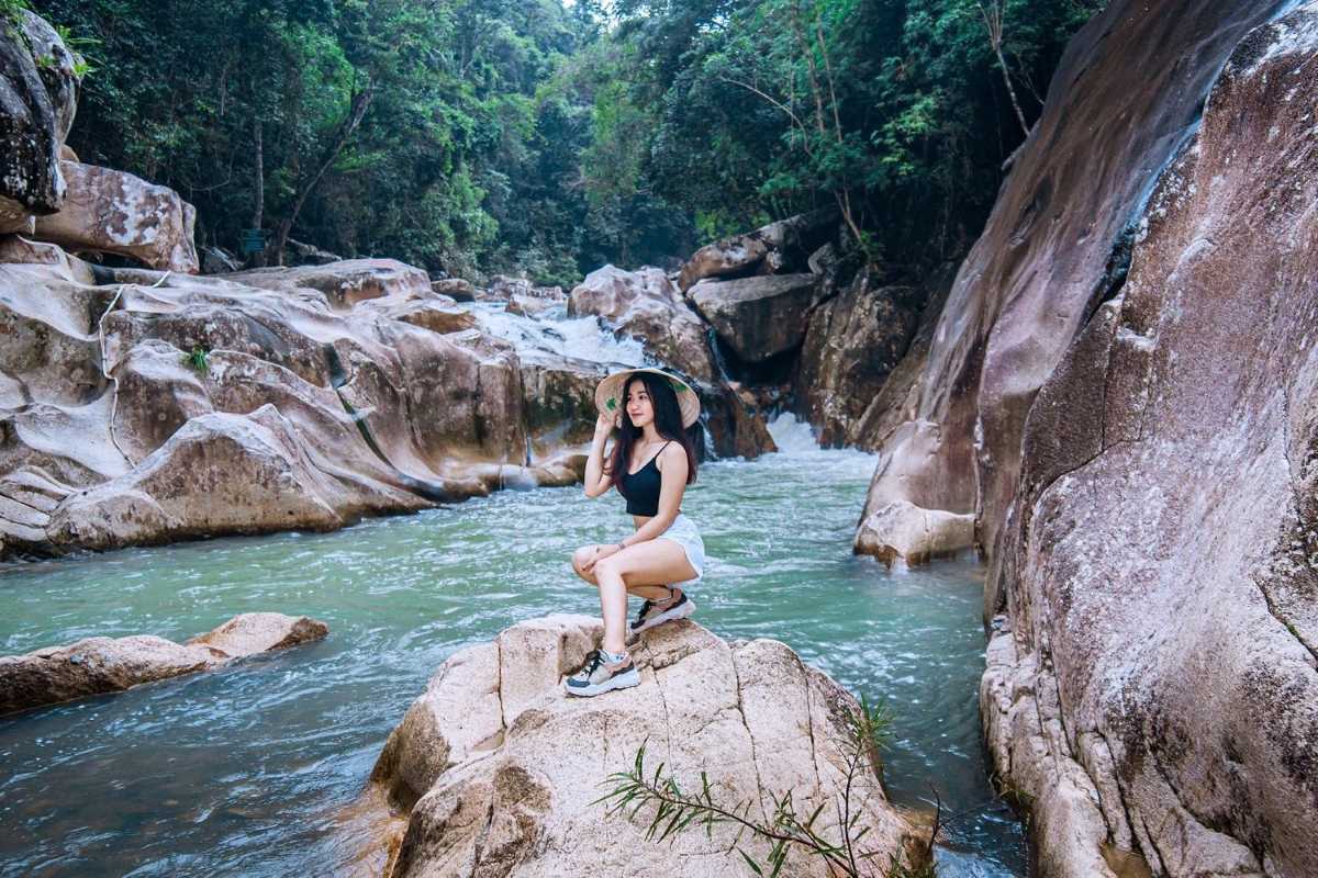 Visitor enjoying Ba Ho stream edge Young woman in hat posing on a rock beside the water at Ba Ho Waterfalls.