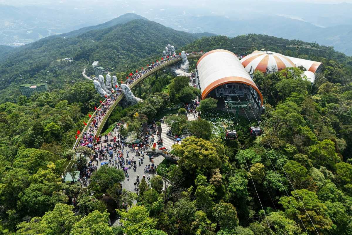 Ba Na Hills Da Nang Golden Bridge aerial view with cable car Ba Na Hills Golden Bridge curves above lush forest with cable cars arriving at mountain station and large crowds