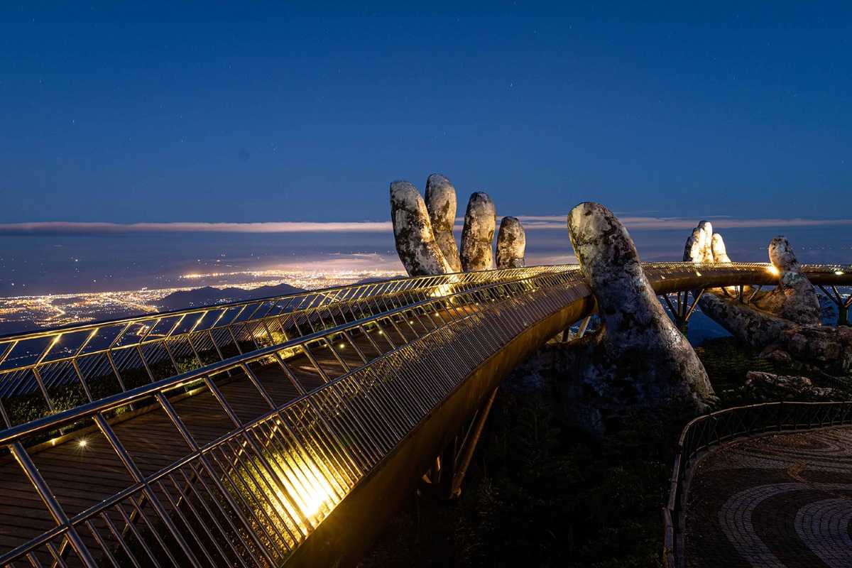 Ba Na Hills Golden Bridge night illuminated mountain landscape Golden Bridge at Ba Na Hills illuminated at night, arching above forested mountain landscape under clear sky