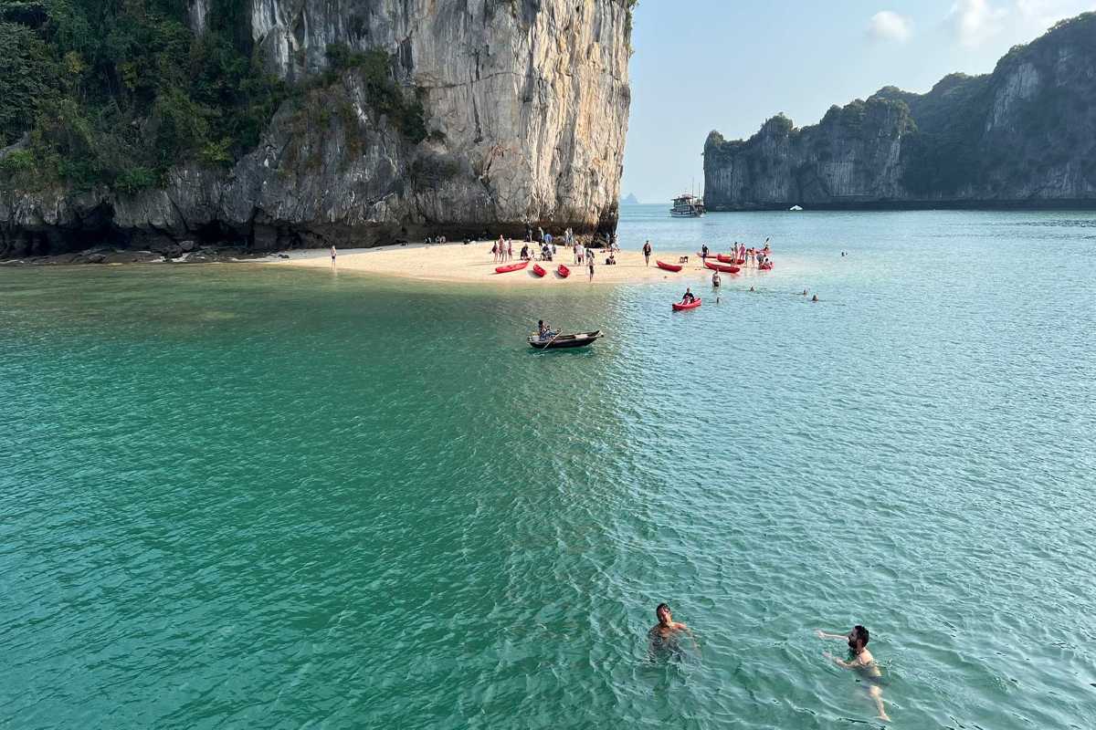 Ba Trai Dao Beach Halong Bay kayaking and swimming adventure Kayakers and swimmers enjoy Ba Trai Dao Beach Halong Bay, surrounded by towering limestone cliffs and emerald water.