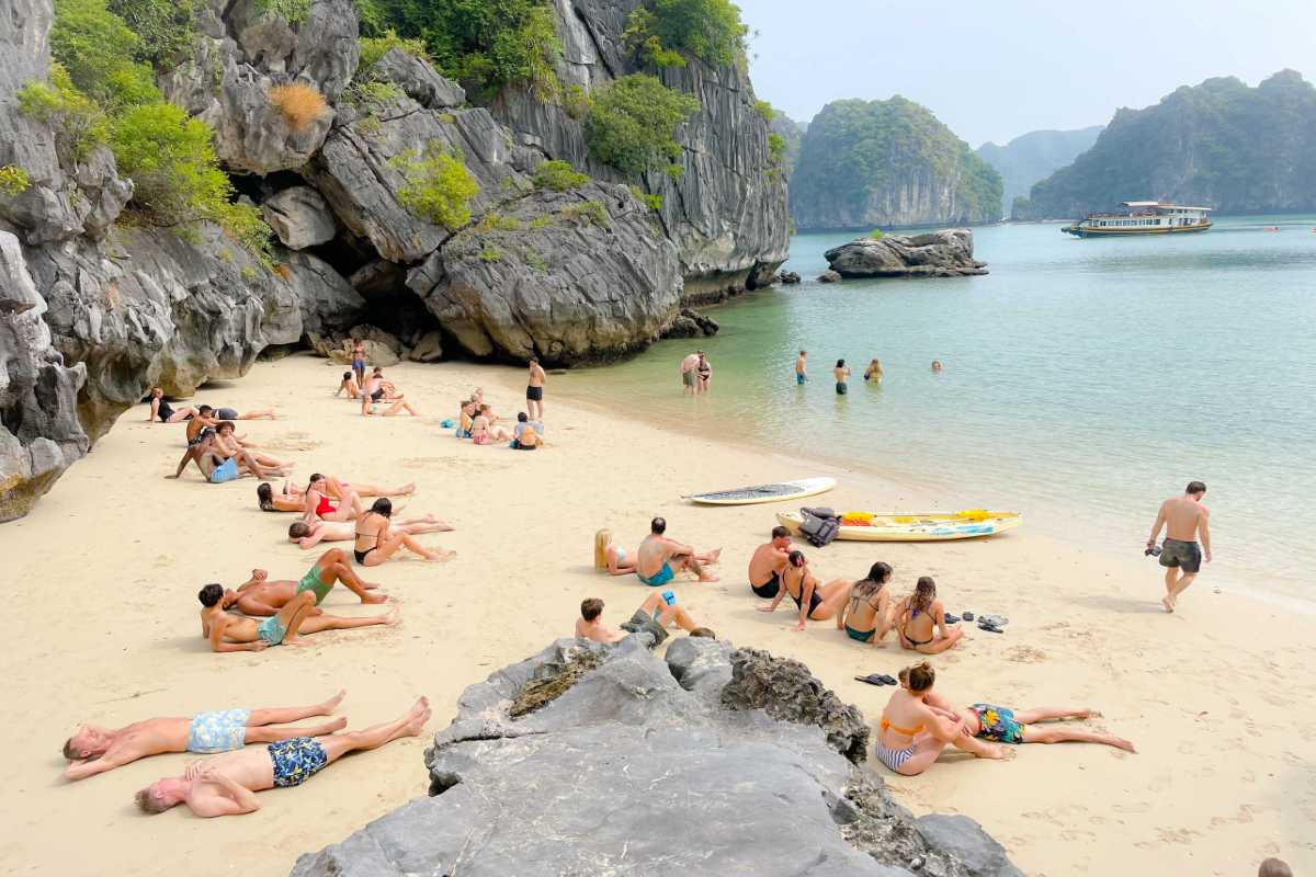 Ba Trai Dao Beach Halong Bay relaxing on sandy beach Travelers relax and sunbathe on the sandy beach at Ba Trai Dao Beach Halong Bay with rocky cliffs and blue water.