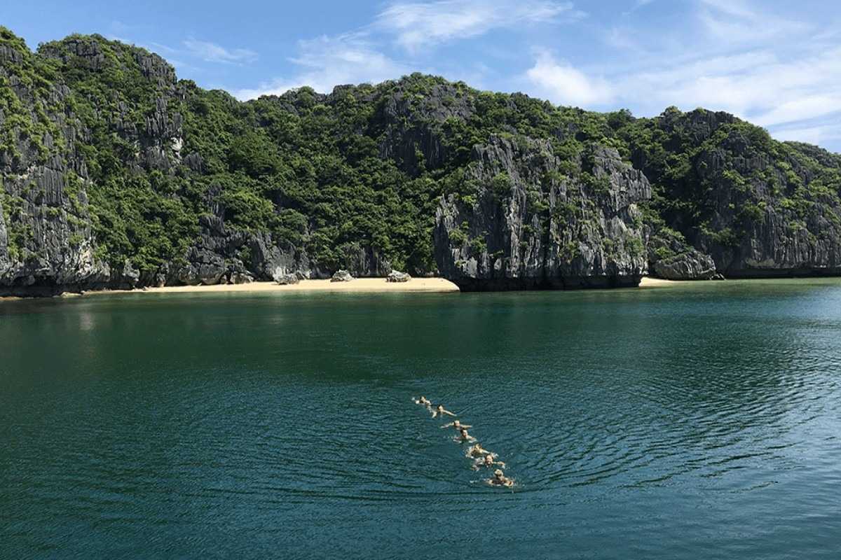 Ba Trai Dao Beach Halong Bay scenic shoreline and swimmers Swimmers enjoy the quiet shoreline at Ba Trai Dao Beach Halong Bay surrounded by green limestone hills.