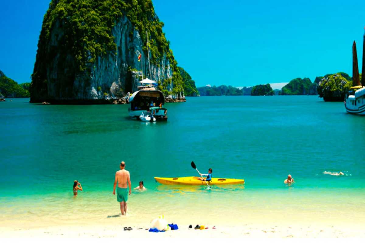 Ba Trai Dao Beach Halong Bay swimming and yellow kayak view Ba Trai Dao Beach Halong Bay displays beachgoers and a yellow kayak with towering cliffs and turquoise water.