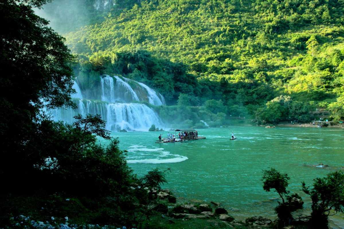 Raft Tour at Scenic Waterfall in Bach Ma National Park Group of tourists on a bamboo raft near a large cascading waterfall in lush greenery