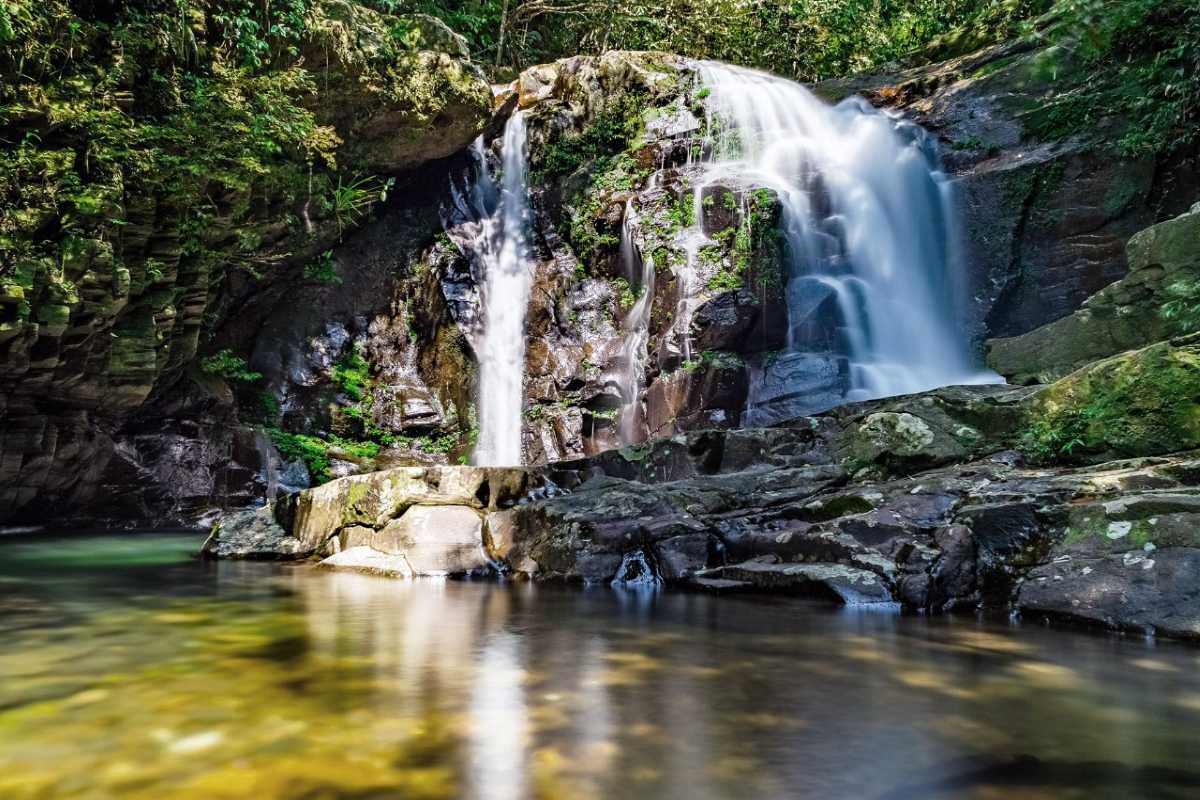 Majestic Bach Ma Waterfall Amid Forest Canopy Wide view of a large waterfall flowing down a rocky cliff into a forested valley at Bach Ma National Park