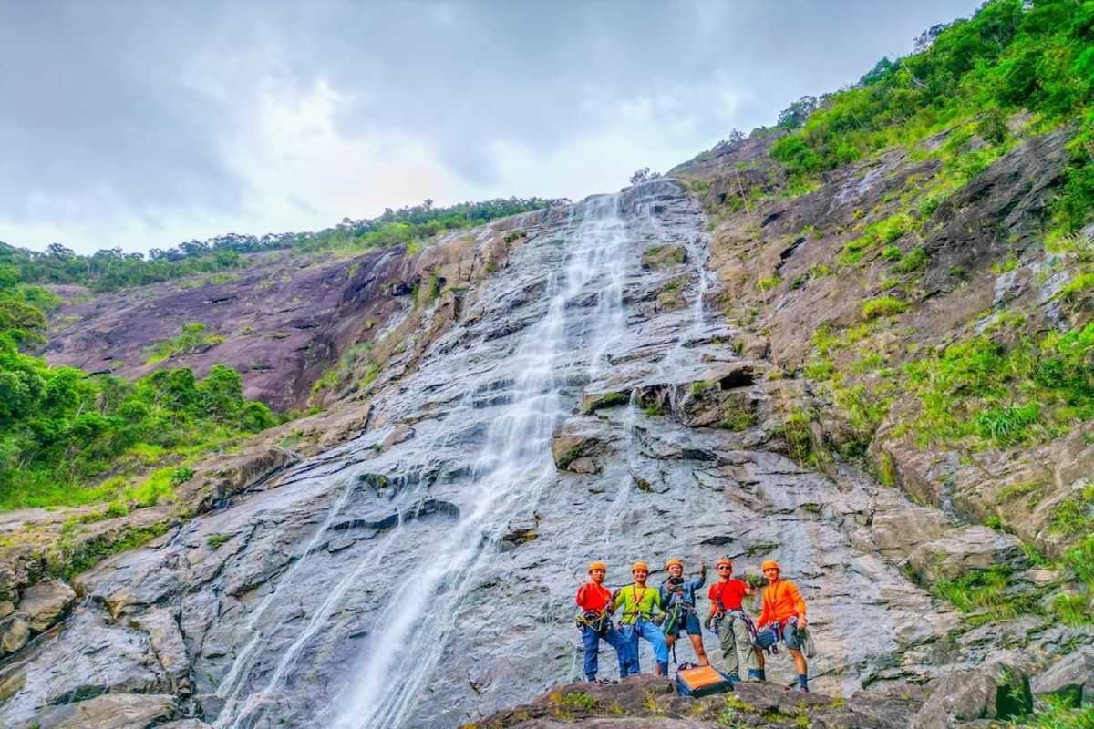Group Rappelling Down Majestic Bach Ma Waterfall Group of climbers preparing for rappelling on a tall waterfall cliff surrounded by dense greenery in Bach Ma National Park