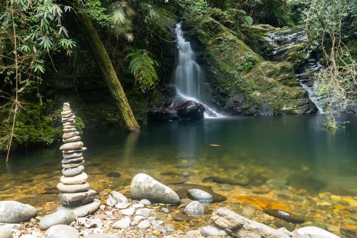 Serene Waterfall and Stone Stack at Bach Ma National Park Tranquil waterfall cascading into a clear pool surrounded by lush forest and balanced stones at Bach Ma National Park