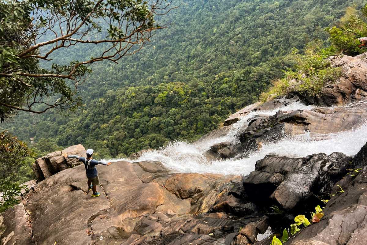 Adventurous Trekking at Bach Ma National Park Waterfall Trekker standing at the edge of a rocky waterfall overlook with dense forest background at Bach Ma National Park