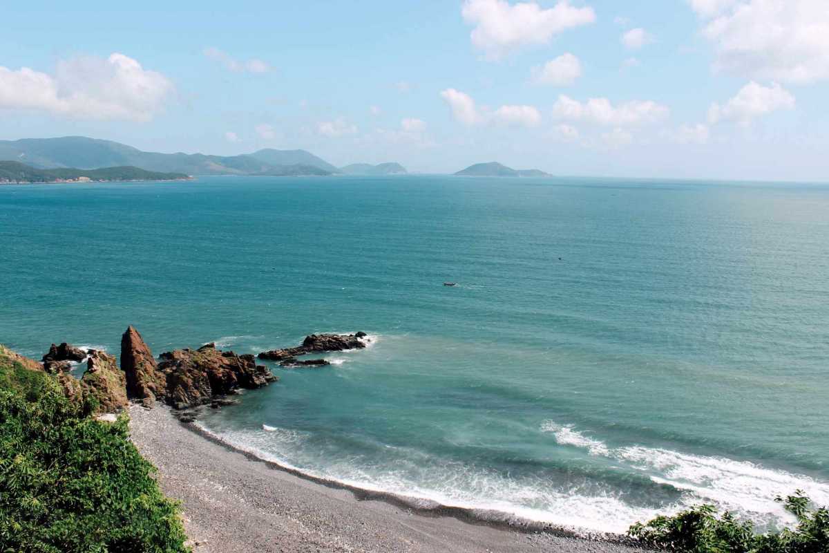 Rocky Coastline at Bai Dai Beach Nha Trang Scenic rocky coastline and waves crashing on Bai Dai Beach Nha Trang's natural shoreline with lush green hills.