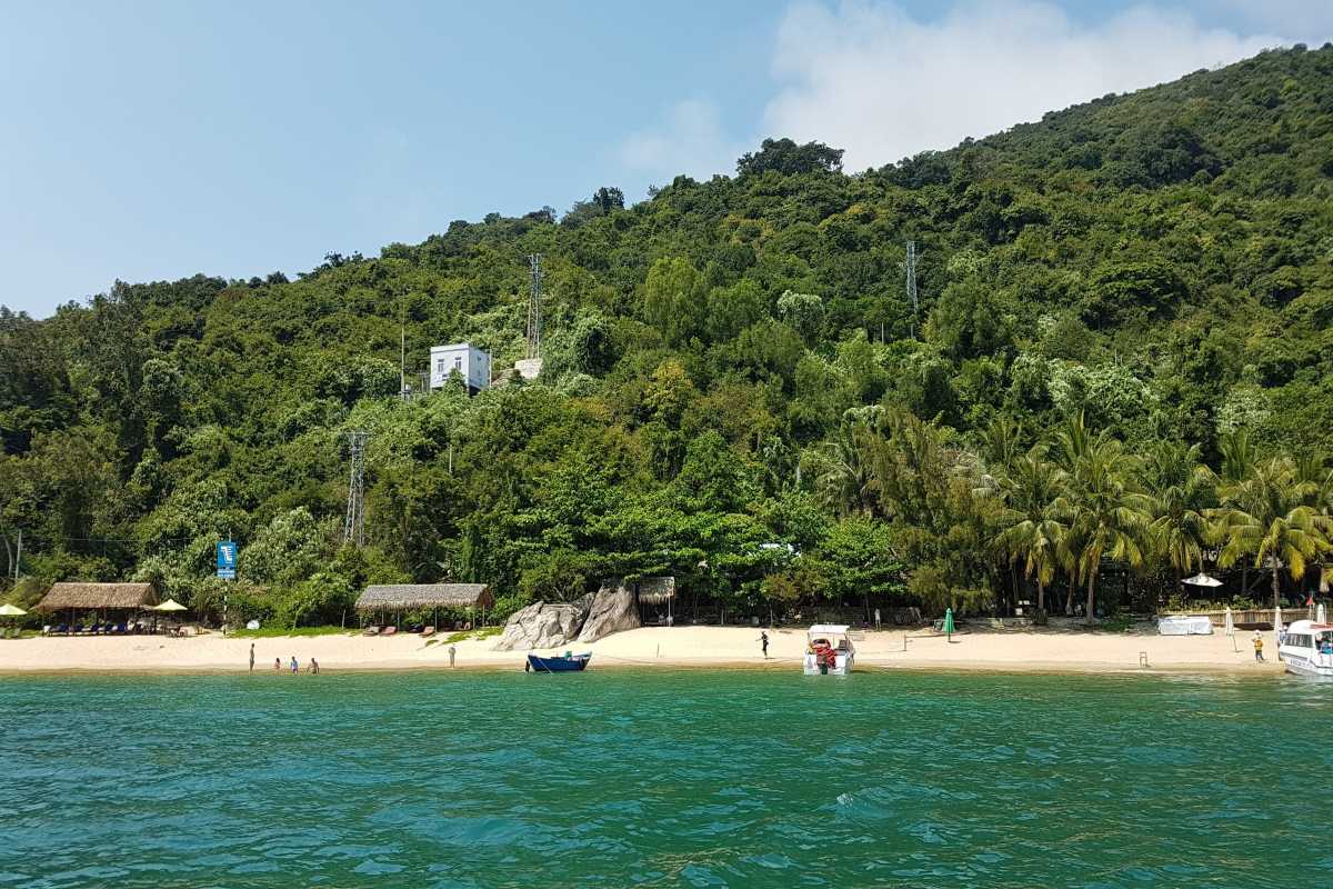 Bai Ong Beach Shoreline and Clear Blue Waters View of Bai Ong Beach with clear blue waters and small boats docked at the shoreline on Cham Islands