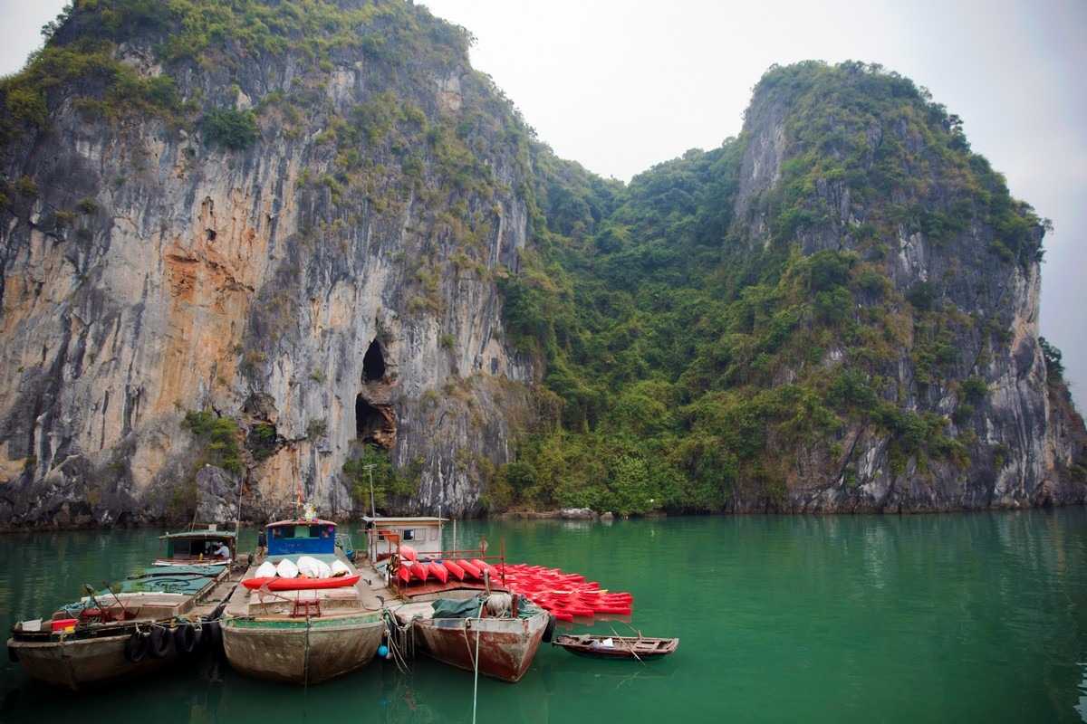Bai Tu Long Bay Vietnam limestone cliff kayak base Kayak base station with red kayaks docked near limestone cliffs in Bai Tu Long Bay Vietnam’s tranquil waters.