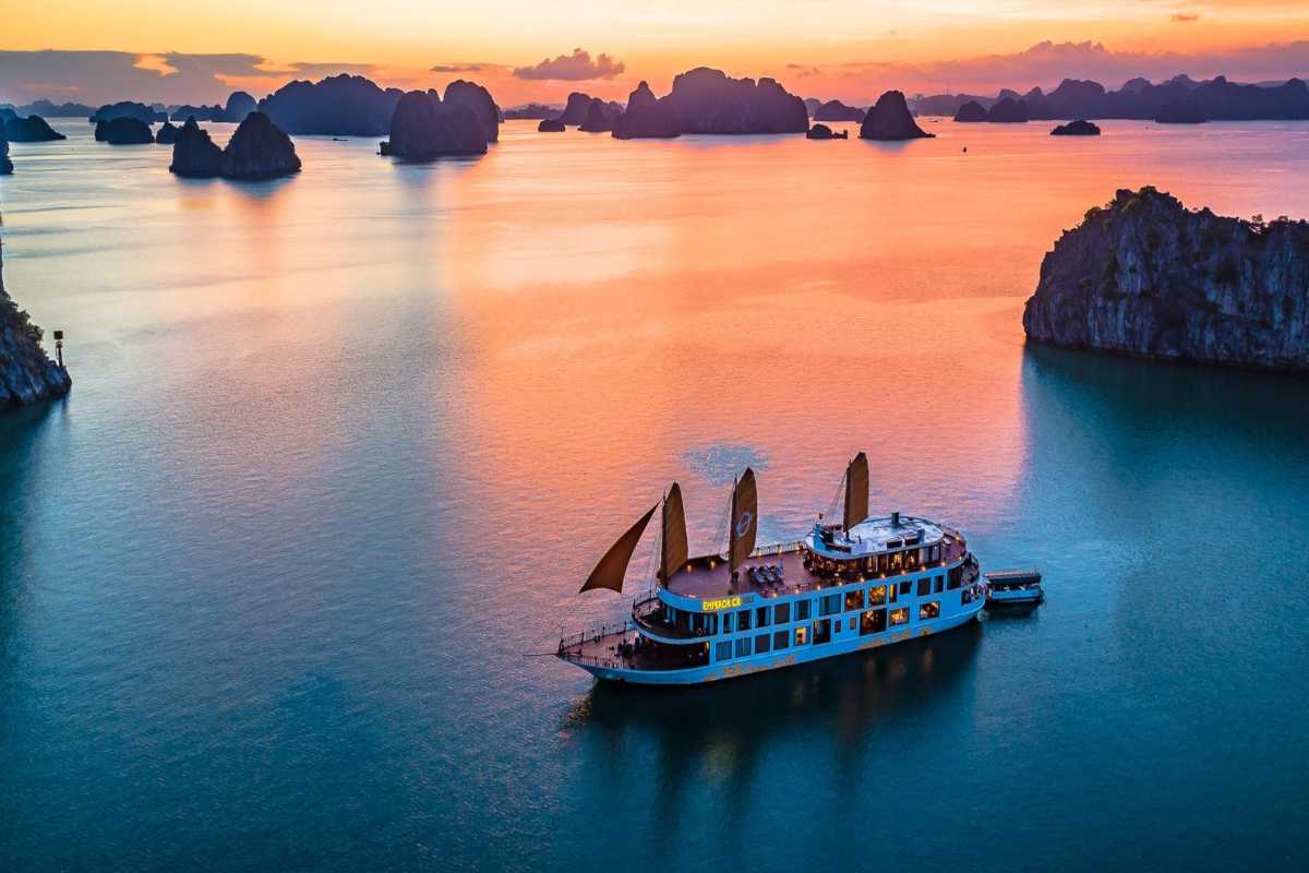 Bai Tu Long Bay Vietnam sunset cruise boat Bai Tu Long Bay Vietnam at sunset with a cruise boat sailing through limestone islands and calm orange waters.