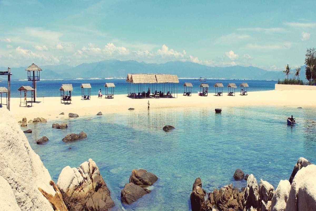 Beachfront Cabanas on Yen Island Wooden cabanas line the clear white sand of Yen Island’s beach, backed by blue sea and distant mountains.