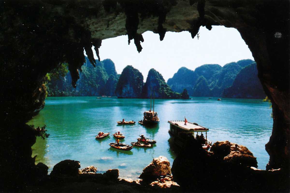 Bo Nau Cave Halong Bay entrance with a boat approaching Bo Nau Cave Halong Bay entrance framed by towering limestone cliffs and surrounded by calm waters.