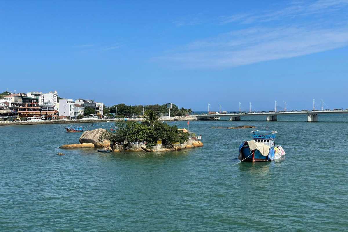 Fishing Boats and Rock Shrine on the Cai River A close-up view of anchored fishing boats near a small rocky island shrine on the Cai River in Nha Trang.