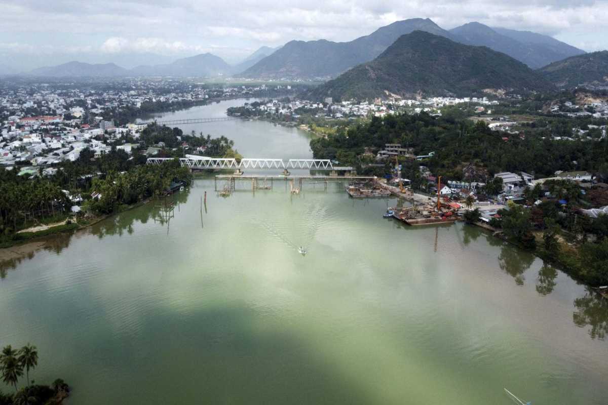 Rail Bridge and Urban Backdrop on Cai River Construction cranes and a rail bridge span the Cai River, with green hills and towns on both banks in Nha Trang.