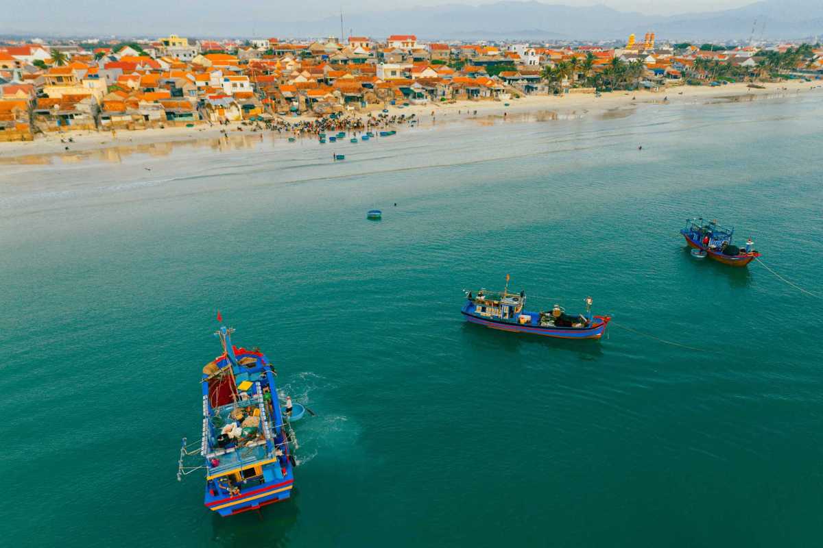Fishing boats on calm waters off Ninh Thuy Fishing Village coastline Fishing boats float on calm waters near the coast of Ninh Thuy Fishing Village with green hills in the distance