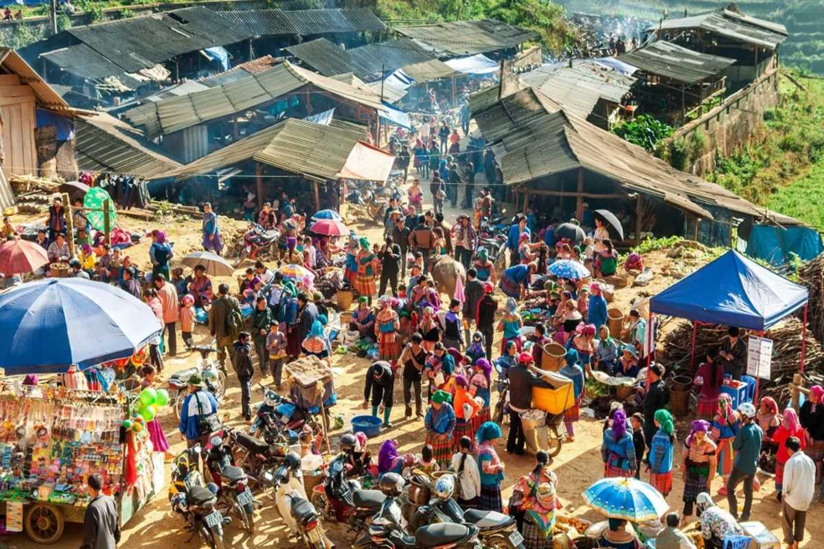 Can Cau Market Lao Cai local crowd with motorbikes and stalls Shoppers navigate through Can Cau Market’s busy paths filled with goods, motorbikes, and ethnic traders