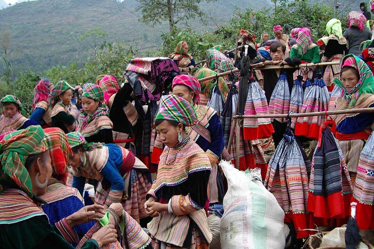 Can Cau Market Lao Cai traditional skirts displayed outdoors Rows of handmade ethnic skirts hang on bamboo racks surrounded by traders at Can Cau Market Lao Cai
